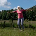 Frau dreht sich mit ausgebreiteten Armen um sich selbst, draußen auf einem Feld