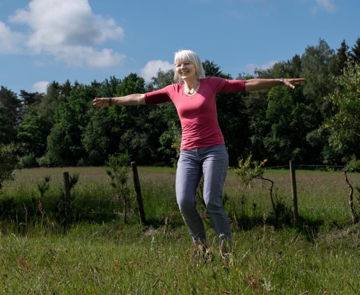 Frau dreht sich mit ausgebreiteten Armen um sich selbst, draußen auf einem Feld