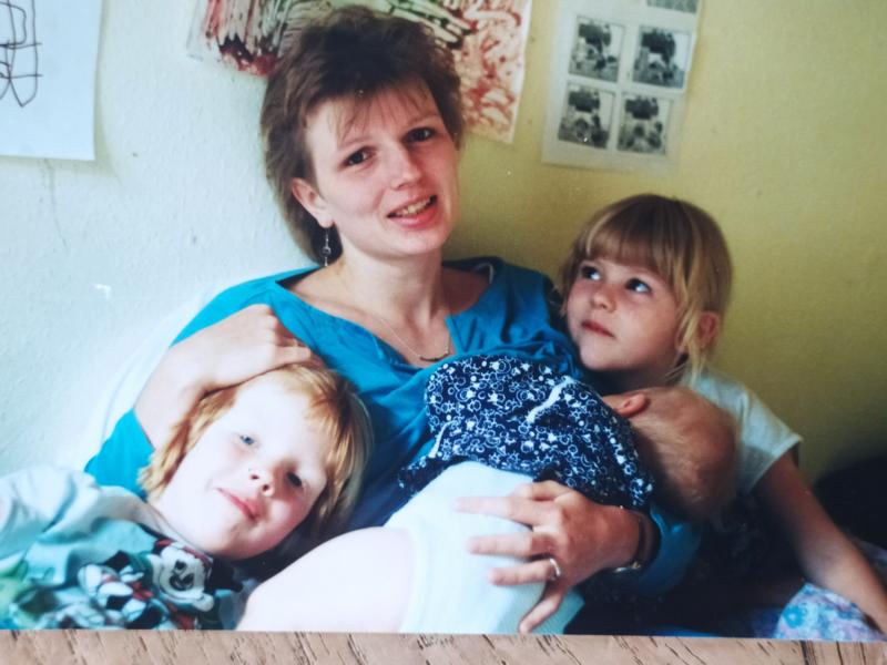 Sitzende Frau mit Baby auf dem Arm und zwei Kindern, rechts und links von ihr.