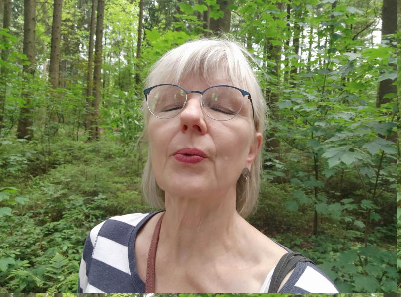 Frau, die mit gespitzten Lippen ausatmet. Sie steht im Wald und hat die Augen geschlossen. So wird das Waldbaden noch effektiver.