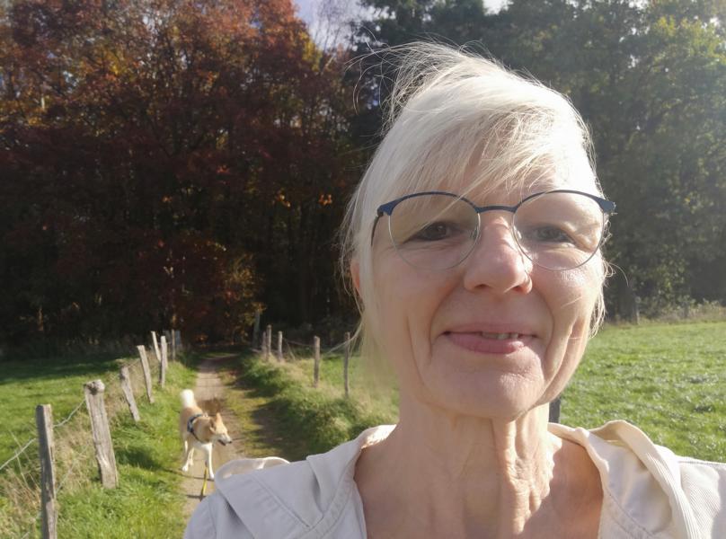 Frau in der Natur mit Hund im Hintergrund